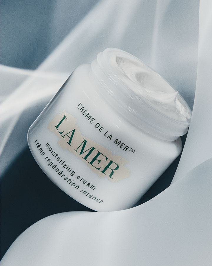 Crème de la Mer Moisturizing Cream with lid off showcasing product texture in a dramatically lit setting